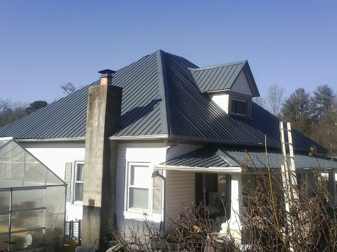 Dark blue standing seam metal roof on a white farmhouse with dormer — Slate & Tile Roof Repair by Roofing Brothers in Buena Park