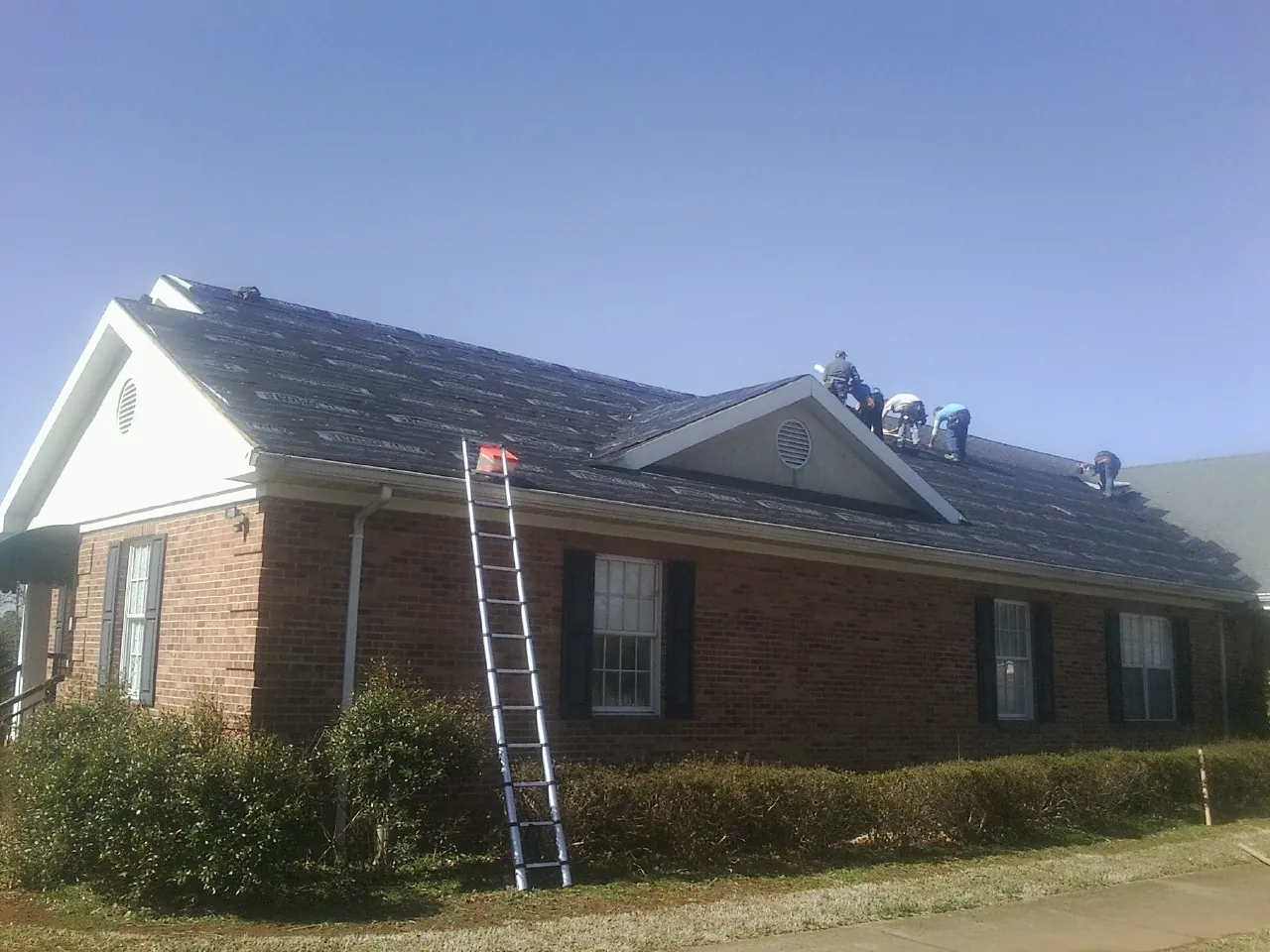 Crew tearing shingles off a brick ranch roof with a ladder set — Emergency Roof Repair work by our crew in Buena Park