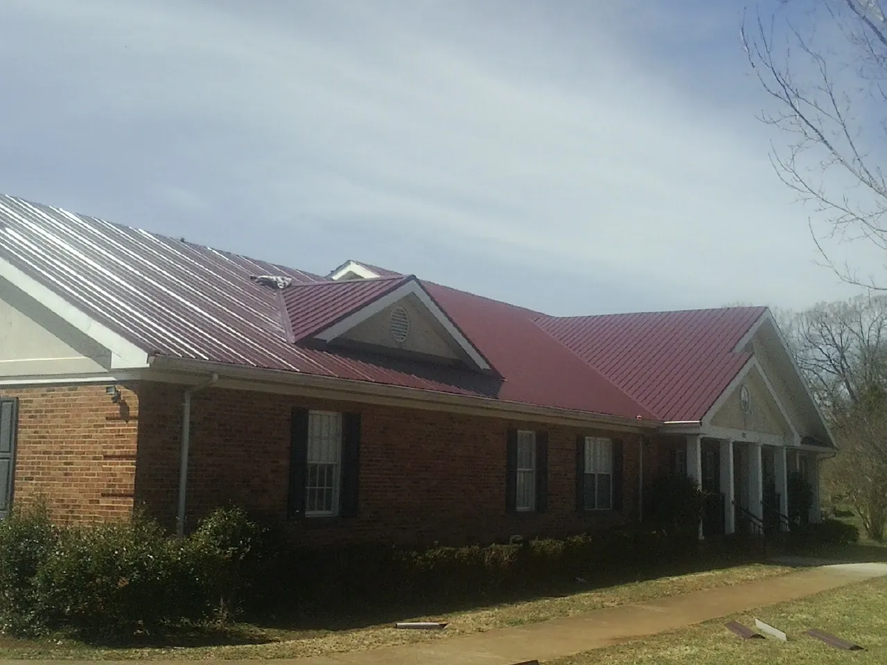 Red metal roof with gabled entries on a long brick building, from a Hail Damage Roof Repair job in Buena Park