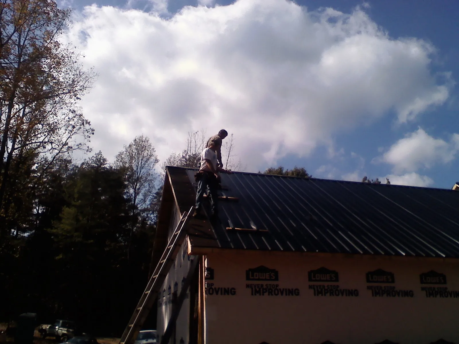Roofer fastening dark metal panels high against a cloudy sky, from a Roof Inspection job in Buena Park