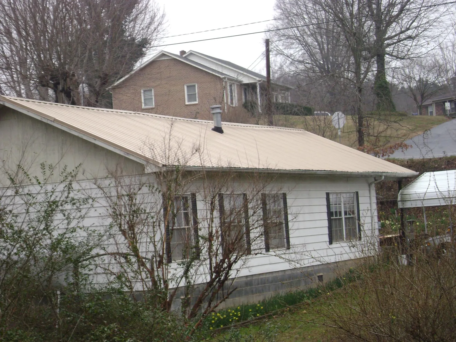Tan metal roof on a white sided house set into a hillside — Commercial Roofing by Roofing Brothers in Buena Park